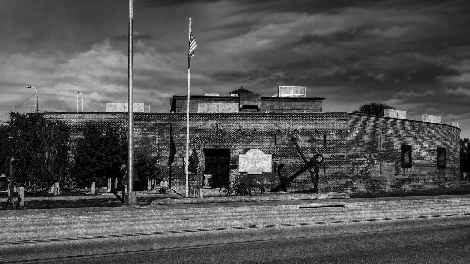 Monochrome editorial rendering of Fort East Martello's brick exterior, flagpoles and displayed anchor.